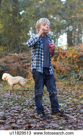Stock Image - Boy blowing bubbles in forest. Fotosearch