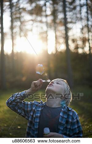 Stock Image - Boy blowing bubbles in forest. Fotosearch