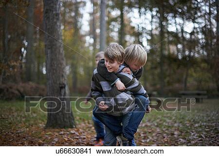 Boy giving friend a piggyback through forest View Large Photo Image Stock Image - Boy giving friend a piggyback through forest. Fotosearch