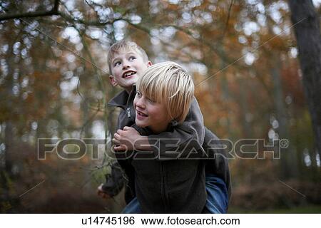 Boy giving friend a piggyback through forest View Large Photo Image Stock Photograph - Boy giving friend a piggyback through forest. Fotosearch