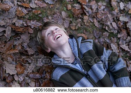 Stock Image - Boy lying on back on forest floor. Fotosearch