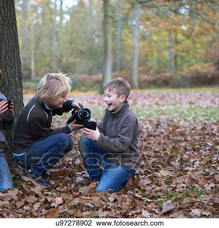 Stock Image - Boys pouring hot drink from flask in forest. Fotosearch