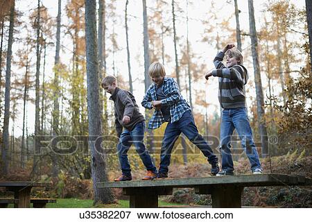 Stock Photo - Boys standing on bench in forest dancing. Fotosearch