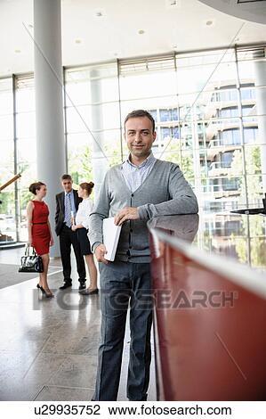Businessman holding laptop leaning against reception desk View Large Photo Image Stock Image - Businessman holding laptop leaning against reception desk. Fotosearch