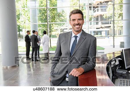 Stock Photo - Businessman leaning against reception desk smiling widely. Fotosearch