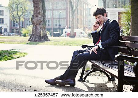 Stock Photo - Businessman on park bench on cell phone. Fotosearch