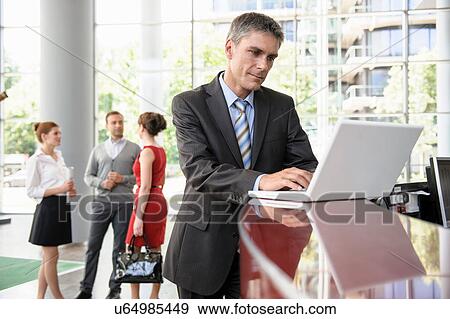 Businessman using laptop on reception desk View Large Photo Image Stock Photo - Businessman using laptop on reception desk. Fotosearch