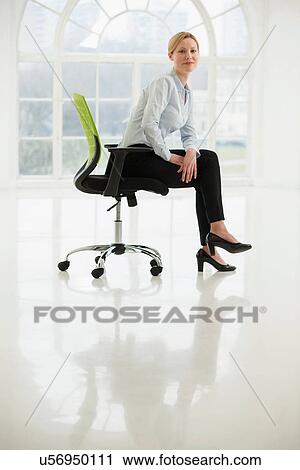 Stock Image - Businesswoman sitting on office chair in sparse white room. Fotosearch