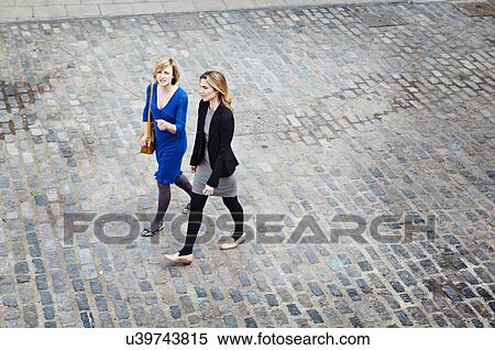 Stock Photography - Businesswomen walking on cobbled street, high angle. Fotosearch