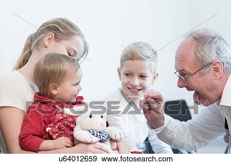 Stock Photo - Child on sister's lap being examined by doctor. Fotosearch