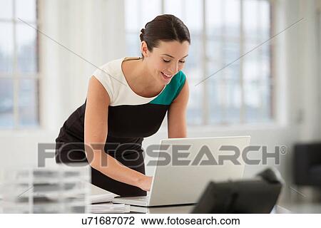 Stock Image - Female office worker using laptop. Fotosearch