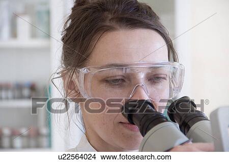 Picture - Female scientist looking through microscope. Fotosearch