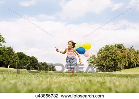 Stock Image - Girl holding balloons running on grass. Fotosearch
