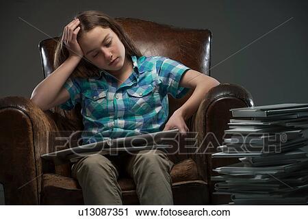 Stock Image - Girl sitting in leather armchair with piles of books. Fotosearch