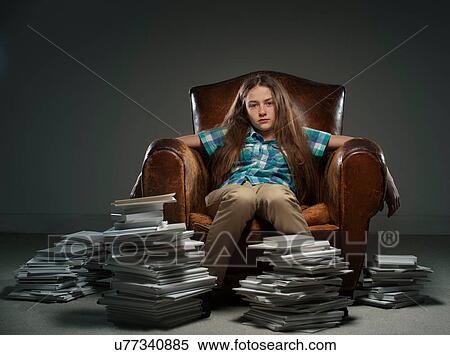 Stock Photography - Girl sitting in leather armchair with piles of books. Fotosearch