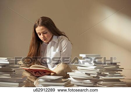 Stock Photo - Girl sitting on floor reading surrounded by piles of books. Fotosearch