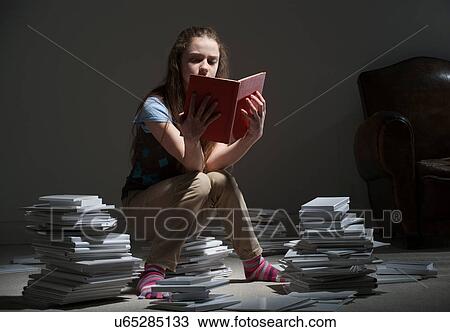 Stock Image - Girl sitting on pile of books reading. Fotosearch