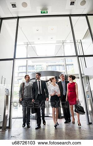 Stock Image - Group of business people talking and entering into glass office building. Fotosearch