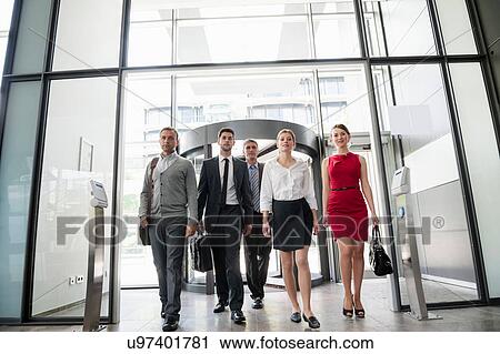 Stock Image - Group of business people walking into glass office building. Fotosearch