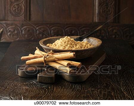 Stock Image - Ingredients for dry cure sugar glazed gammon joint. Cinnamon sticks tied with string and brown sugar in wooden bowl. Fotosearch