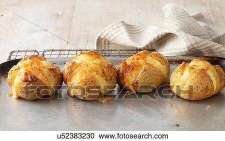 Stock Image - Jacket potatoes baked in oven with cheese on metal baking tray. Fotosearch