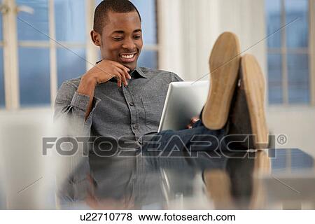 Stock Photo - Male office worker sitting at desk with feet up. Fotosearch