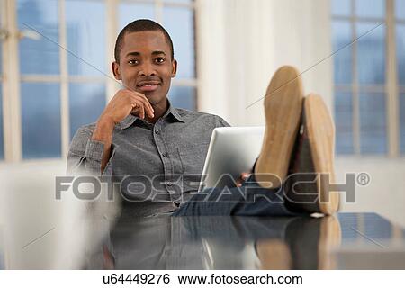 Male office worker sitting at desk with feet up View Large Photo Image Stock Photograph - Male office worker sitting at desk with feet up. Fotosearch