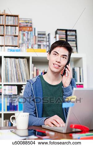 Picture - Male student on cell phone using laptop. Fotosearch