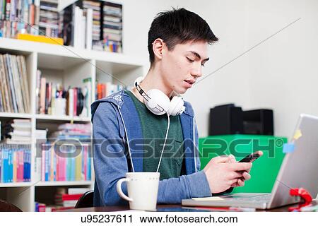 Male student using cell phone at desk View Large Photo Image Stock Image - Male student using cell phone at desk. Fotosearch