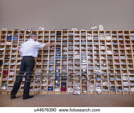 Stock Image - Man selecting fabric samples from shelving unit. Fotosearch