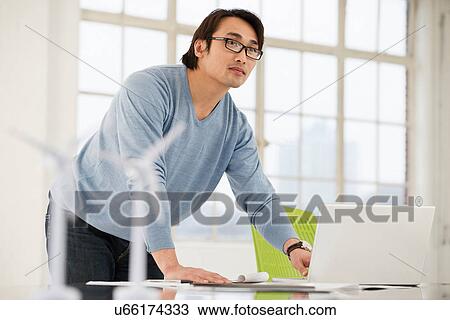 Stock Image - Man using laptop with models of wind turbines on desk. Fotosearch