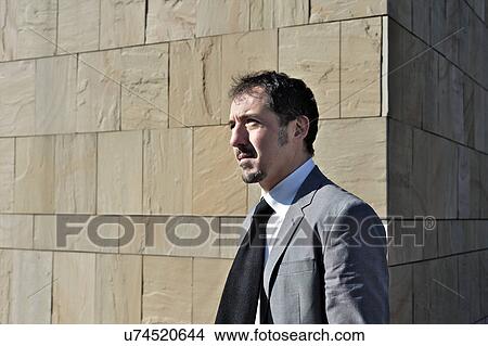 Picture - Mature businessman standing by brick wall outdoors. Fotosearch