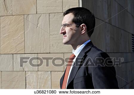Stock Image - Mature businessman standing by brick wall outdoors. Fotosearch