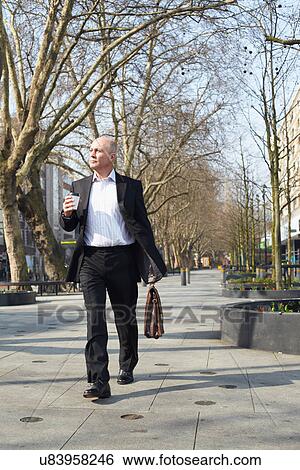 Stock Photograph - Mature businessman walking on sidewalk with coffee. Fotosearch