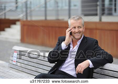 Mature man making cellphone call on bench View Large Photo Image Stock Image - Mature man making cellphone call on bench. Fotosearch