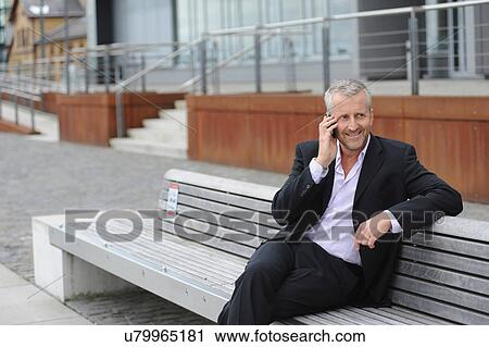 Mature man making cellphone call on bench View Large Photo Image Stock Image - Mature man making cellphone call on bench. Fotosearch