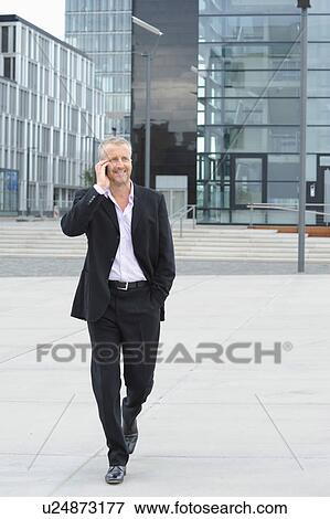 Stock Photo - Mature man walking in financial district and using cellphone. Fotosearch