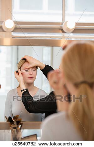 Stock Image - Mid adult woman having make-up applied. Fotosearch