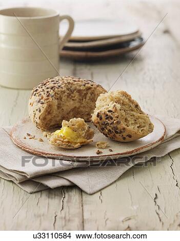 Picture - Mixed seed bread roll with butter. Sunflower seeds, poppy seeds and flax seeds. Fotosearch