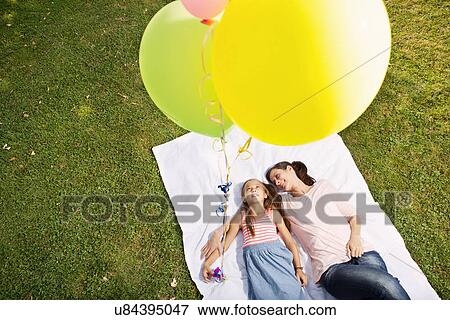 Mother and daughter lying on blanket holding balloons, high angle View Large Photo Image Stock Photo - Mother and daughter lying on blanket holding balloons, high angle. Fotosearch