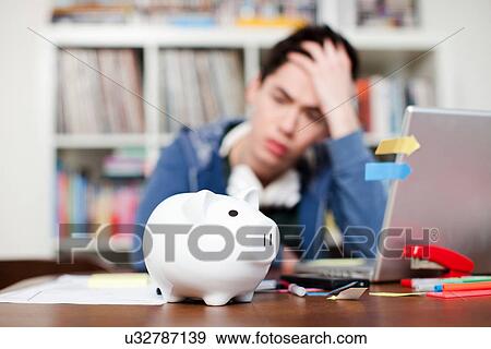 Stock Photo - Piggy bank with young man worrying in background. Fotosearch