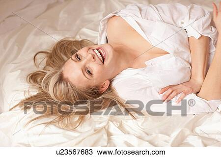 Stock Image - Portrait of a young blond woman lying on bed smiling. Fotosearch