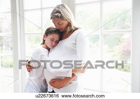 Stock Photograph - Pregnant mother with teenage daughter by window. Fotosearch