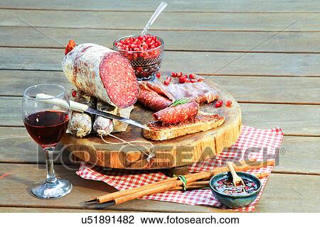 Stock Image - Salami on chopping board with wine and condiments. Fotosearch