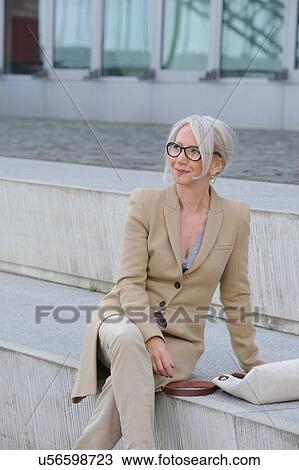 Stock Image - Senior woman sitting on steps in city. Fotosearch