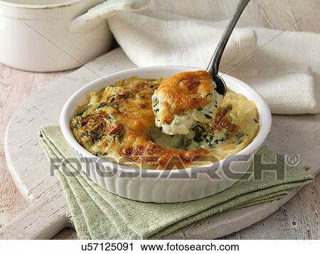 Stock Image - Spinach gratin in a white dish with metal spoon on green cloth. Fotosearch