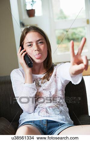 Teenage girl on phone making peace sign with tongue out View Large Photo Image Picture - Teenage girl on phone making peace sign with tongue out. Fotosearch