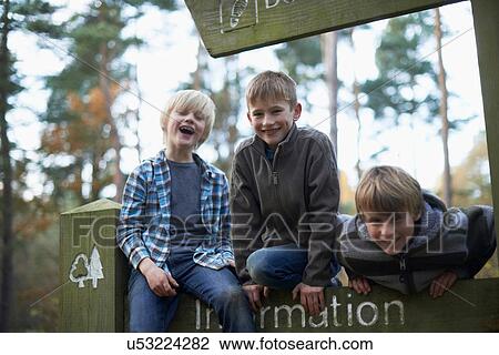 Stock Image - Three boys climbing on sign in forest. Fotosearch