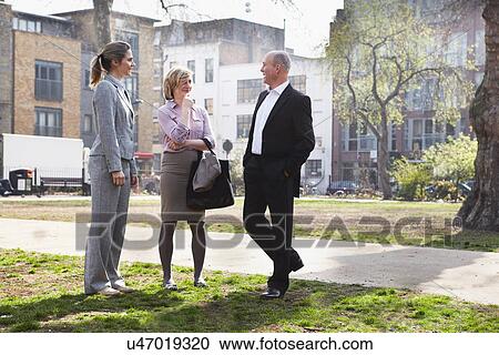 Stock Image - Three businesspeople standing talking in park. Fotosearch