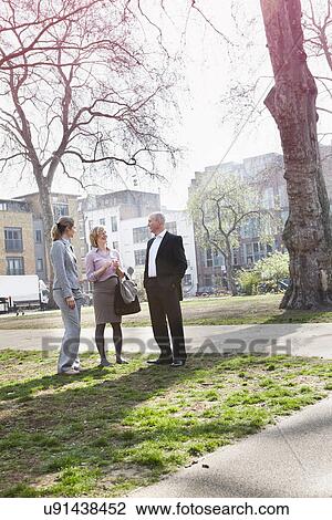 Stock Image - Three businesspeople standing talking in park. Fotosearch